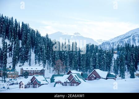 Blick auf verschneite Häuser und Berge in Gulmarg. Gulmarg ist eine Stadt, eine Bergstation, ein beliebtes Skiziel und ein mitteiltes Gebietskomitee im Baramulla Distrikt Jammu und Kaschmir. Die Stadt liegt in der Pir Panjal Range im westlichen Himalaya und liegt innerhalb der Grenzen des Gulmarg Wildlife Sanctuary. Stockfoto