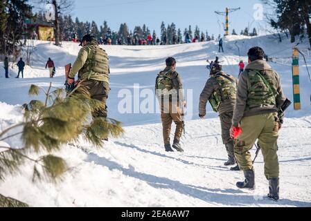 Indische Polizisten gehen auf einer schneebedeckten Wiese in Gulmarg entlang. Gulmarg ist eine Stadt, eine Bergstation, ein beliebtes Skiziel und ein mitteiltes Gebietskomitee im Baramulla Distrikt Jammu und Kaschmir. Die Stadt liegt in der Pir Panjal Range im westlichen Himalaya und liegt innerhalb der Grenzen des Gulmarg Wildlife Sanctuary. Stockfoto