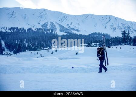 Ein Skifahrer spaziert auf einer schneebedeckten Wiese in Gulmarg. Gulmarg ist eine Stadt, eine Bergstation, ein beliebtes Skiziel und ein mitteiltes Gebietskomitee im Baramulla Distrikt Jammu und Kaschmir. Die Stadt liegt in der Pir Panjal Range im westlichen Himalaya und liegt innerhalb der Grenzen des Gulmarg Wildlife Sanctuary. Stockfoto