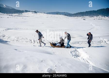 Ein Mann zieht mit den Touristen im berühmten Skigebiet in Gulmarg einen Schlitten. Gulmarg ist eine Stadt, eine Bergstation, ein beliebtes Skiziel und ein mitteiltes Gebietskomitee im Baramulla Distrikt Jammu und Kaschmir. Die Stadt liegt in der Pir Panjal Range im westlichen Himalaya und liegt innerhalb der Grenzen des Gulmarg Wildlife Sanctuary. Stockfoto