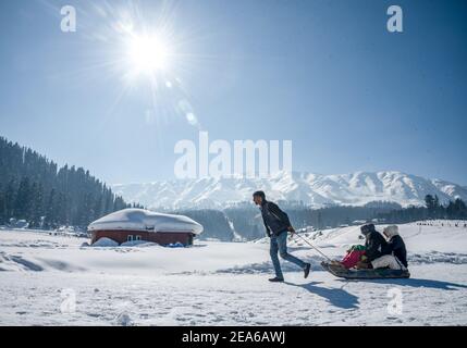Ein Mann zieht den Schlitten mit Touristen im berühmten Skigebiet in Gulmarg. Gulmarg ist eine Stadt, eine Bergstation, ein beliebtes Skiziel und ein mitteiltes Gebietskomitee im Baramulla Distrikt Jammu und Kaschmir. Die Stadt liegt in der Pir Panjal Range im westlichen Himalaya und liegt innerhalb der Grenzen des Gulmarg Wildlife Sanctuary. Stockfoto
