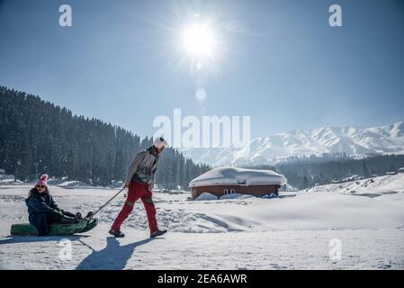 Ein Mann zieht einen Schlitten mit Touristen in berühmten Skigebiet in Gulmarg. Gulmarg ist eine Stadt, eine Bergstation, ein beliebtes Skiziel und ein mitteiltes Gebietskomitee im Baramulla Distrikt Jammu und Kaschmir. Die Stadt liegt in der Pir Panjal Range im westlichen Himalaya und liegt innerhalb der Grenzen des Gulmarg Wildlife Sanctuary. Stockfoto