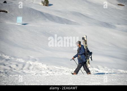 Ein Mann läuft auf einer schneebedeckten Wiese in Gulmarg. Gulmarg ist eine Stadt, eine Bergstation, ein beliebtes Skiziel und ein mitteiltes Gebietskomitee im Baramulla Distrikt Jammu und Kaschmir. Die Stadt liegt in der Pir Panjal Range im westlichen Himalaya und liegt innerhalb der Grenzen des Gulmarg Wildlife Sanctuary. Stockfoto