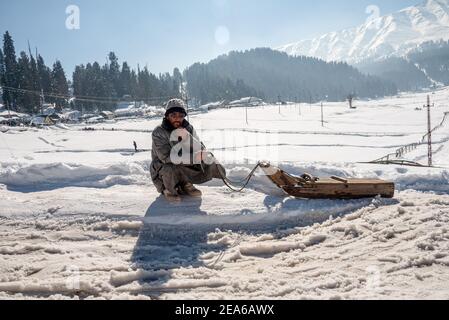 Ein Schlittenbesitzer wartet auf Kunden in einem berühmten Skigebiet in Gulmarg. Gulmarg ist eine Stadt, eine Bergstation, ein beliebtes Skiziel und ein mitteiltes Gebietskomitee im Baramulla Distrikt Jammu und Kaschmir. Die Stadt liegt in der Pir Panjal Range im westlichen Himalaya und liegt innerhalb der Grenzen des Gulmarg Wildlife Sanctuary. Stockfoto