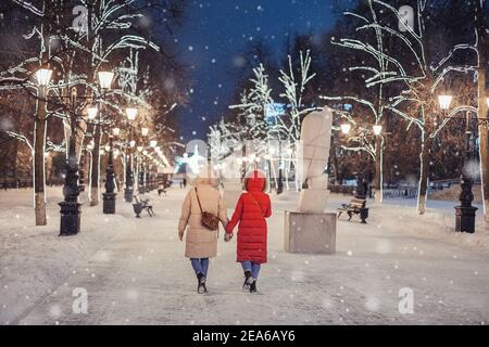 Glückliche Freundinnen gehen im abendlichen Winterpark auf dem Bürgersteig vor dem Hintergrund der Weihnachts- und Neujahrsdekorationen in Ufa, Russland Stockfoto