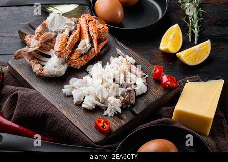 Spanische oder thailändische Omelette Zutat, frische rote Chili, braun und weiß Krabbenfleisch, Zitrone, Cheddar-Käse, Eier-Set, auf dunklem Holzhintergrund Stockfoto