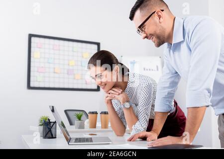 Glückliche Geschäftsleute, die sich einen Laptop am Schreibtisch angeschaut haben Stockfoto