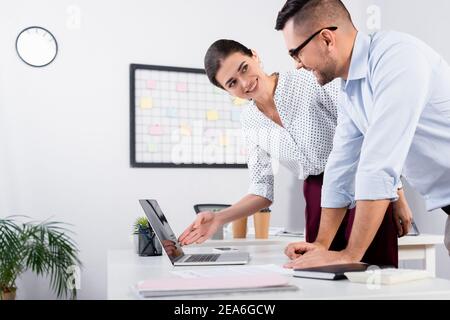 Glückliche Geschäftsfrau zeigt mit der Hand auf Laptop mit leerem Bildschirm Am Schreibtisch Stockfoto