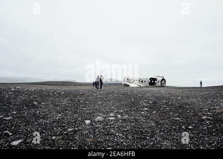 Touristische Wanderer zu den abgelegenen und unheimlichen Dakota Flugzeug Wrack in der schwarzen Sandebene Wüste von Sólheimasandur in Süd-Island. Stockfoto