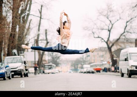 Japanische Ballerina führt Split und Sprünge in der Stadt Straße vor dem Hintergrund der Autos. Stockfoto