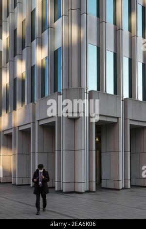 Ein japanischer Büroangestellter oder Salaryman überprüft sein Smartphone, als er aus dem Shinjuku Nomura-Gebäude in Shinjuku, Tokio, Japan, kommt Stockfoto