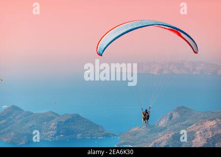 Lehrer und Schüler im Tandem schweben auf einem großen blauen Gleitschirm in die Luft. Berge und Meer im Hintergrund. Positive und scharfe Eindrücke für t Stockfoto