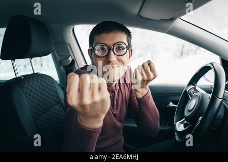 Witziger und lächerlicher Nerd-Fahrer in Brillen, der zur Kamera schreit und seine Faust in einem Auto zeigt. Konzept eines Neuling Fahrer Konflikt und accid Stockfoto