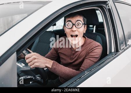 Lächerlicher Geek-Fahrer starrt auf die Kamera und hält das Lenkrad. Konzept eines Anfänger Fahrer und lernen, in der Stadt zu fahren Stockfoto