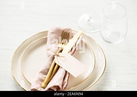 Goldene Rim Teller und goldenes Besteck mit Anhänger auf weißem Tisch gebunden. Winkelansicht auf Tischeinstellung. Stockfoto