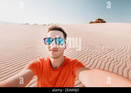 Glücklicher Mann Tramp in Sonnenbrille nimmt ein Selfie-Foto in Die Wüste vor dem Hintergrund einer Düne aus Weiß Sand Stockfoto