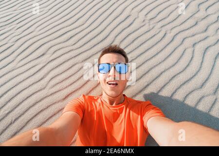 Glücklicher Mann Tramp in Sonnenbrille nimmt ein Selfie-Foto in Die Wüste vor dem Hintergrund einer Düne aus Weiß Sand Stockfoto