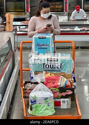FRESNO, USA - 05. Feb 2021: Ein Foto einer jungen Frau mit ihrem großen orangefarbenen Wagen mit Lebensmitteln, die in Costco auf ihr iPhone herabschauen Stockfoto