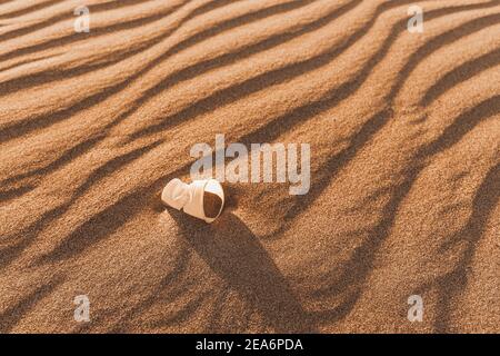 Ein ausrangierte Plastikbecher liegt auf einer Sanddüne in der Wüste. Das Konzept von Umweltproblemen und biologisch abbaubaren chemischen Materialien Stockfoto