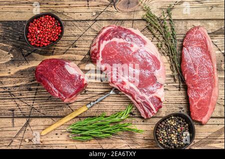 Frisch roh prime schwarz angus Rindfleisch Steaks Filet Mignon, Rib Eye oder Cowboy, Striploin. Holzhintergrund. Draufsicht Stockfoto