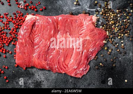 Rohes Flankensteak mit schwarzem und rosa Pfeffer. Schwarzer Hintergrund. Draufsicht Stockfoto