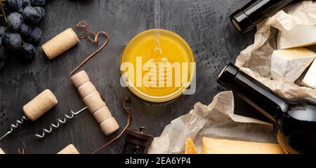 Honig im Glas mit Honiglöffel auf dunklem Steinbrett mit Weinkäse Korkenzieher Trauben . Romantisches Abendessen Weinprobe mit Rotwein Käse Snacks Stockfoto