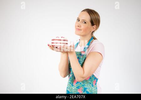 Lächelnd schöne junge Frau trägt Schürze hält kleine Kuchen auf weißem Hintergrund. Stockfoto