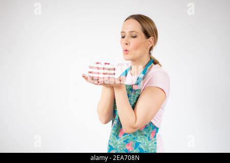Lächelnd schöne junge Frau trägt Schürze hält kleine Kuchen auf weißem Hintergrund. Stockfoto