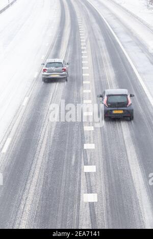 Verschneite Autobahn mit einem einsamen Auto, das durch Schneesturm fährt Stockfoto