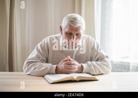 Älterer Mann, der betete und eine alte Bibel in seinen Händen las. Stockfoto