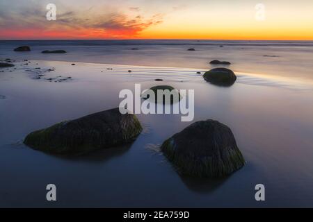 Schöner, farbenfroher Sonnenuntergang über Meer und Felsbrocken. Ostseeküste, Estland. Stockfoto