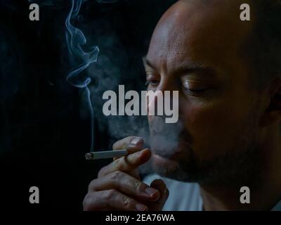 Mann raucht eine Zigarette und bläst weißen Rauch aus. Stockfoto