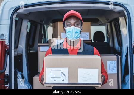 Schwarzer Kurier Mann liefert Paket vor dem Lastenwagen Tragen einer Sicherheitsmaske - Fokus auf das Gesicht Stockfoto