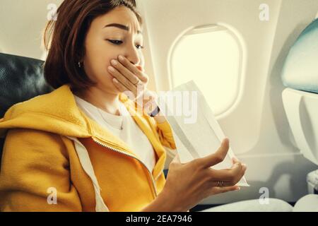 Eine asiatische weibliche Reisende leidet unter einem akuten Angriff von Übelkeit während Turbulenzen auf einem Flugzeug. Die Frau war seekrank und Luftsocke während des Flugs Stockfoto