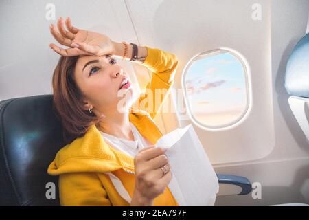 Eine asiatische weibliche Reisende leidet unter einem akuten Angriff von Übelkeit während Turbulenzen auf einem Flugzeug. Die Frau war seekrank und Luftsocke während des Flugs Stockfoto