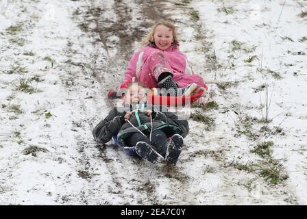 Amy Heather, 10 Jahre (links) und Betty Smith, 7 Jahre, Rodeln in der Nähe der Küste bei Southend-on-Sea in Essex. Das Met Office veröffentlichte schwere bernsteinfarbene Schneewarnungen für London und Südostengland, wo starker Schnee wahrscheinlich zu langen Verzögerungen auf den Straßen und bei Bahn- und Flugreisen führen wird. Bilddatum: Montag, 8. Februar 2021. Stockfoto