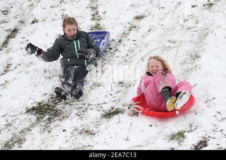 Amy Heather, 10 Jahre (links) und Betty Smith, 7 Jahre, Rodeln in der Nähe der Küste bei Southend-on-Sea in Essex. Das Met Office veröffentlichte schwere bernsteinfarbene Schneewarnungen für London und Südostengland, wo starker Schnee wahrscheinlich zu langen Verzögerungen auf den Straßen und bei Bahn- und Flugreisen führen wird. Bilddatum: Montag, 8. Februar 2021. Stockfoto