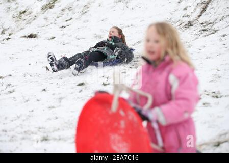 Amy Heather, 10 Jahre (links) und Betty Smith, 7 Jahre, Rodeln in der Nähe der Küste bei Southend-on-Sea in Essex. Das Met Office veröffentlichte schwere bernsteinfarbene Schneewarnungen für London und Südostengland, wo starker Schnee wahrscheinlich zu langen Verzögerungen auf den Straßen und bei Bahn- und Flugreisen führen wird. Bilddatum: Montag, 8. Februar 2021. Stockfoto