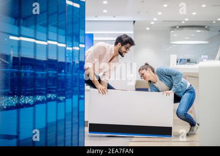 Junges Paar versucht, Aufzug verpackt Plasma-TV. Inneneinrichtung des Technikladens. Stockfoto