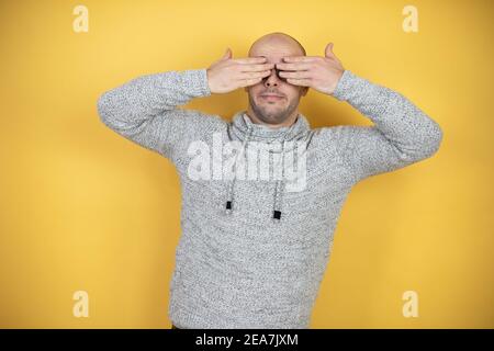 Junge Glatze Mann trägt Brille über gelben Hintergrund Augen mit Händen lächelnd fröhlich und lustig. Blindes Konzept. Stockfoto