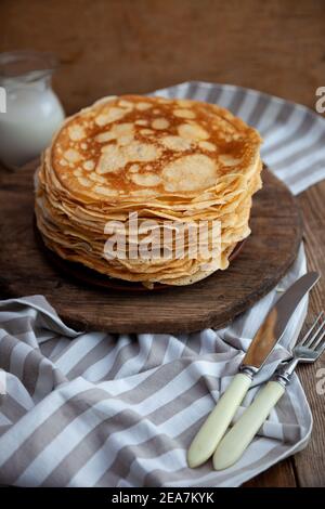 Dünne gebratene Pfannkuchen auf einem Teller. Traditionelles Essen für Fasching. Pfannkuchen mit saurer Sahne auf einem Holztisch Stockfoto