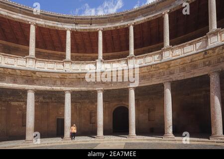 Eine junge blonde Frau, die an einem klaren, sonnigen Tag den runden, runden Innenhof des Palastes von Karl V. in der Alhambra in Granada, Spanien, besichtigt. Stockfoto