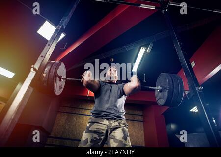 Stark fokussierter bärtiger Mann, der in der dunklen Turnhalle schwere Gewichte hebt. Stockfoto