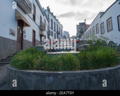 Firgas, Gran Canaria, Kanarische Inseln, Spanien 13. Dezember 2020: Blick auf die Straße Paseo de Gran Canaria mit Wasserfall Brunnen, Blumen und Keramik Stockfoto