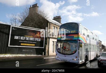 Ein Bus, der mit Regenbogen und NHS-Aufklebern geschmückt ist, fährt an einer Werbeplakette im Zusammenhang mit Coronavirus in Falkirk, Zentralschottland, vorbei, wo die am 5. Januar für das schottische Festland eingeführten Lockdown-Maßnahmen bis mindestens Ende Februar in Kraft bleiben. Bilddatum: Montag, 8. Februar 2021. Stockfoto