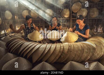 Gruppe von vietnamesischen Kunsthandwerkerinnen Herstellung der traditionellen vietnam Hut in der alten traditionellen Haus in AP Thoi Phuoc Dorf, Hochiminh Stadt, Vietnam Stockfoto