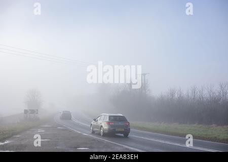 Autos verschwinden in dichtem Nebel. Ein LKW Scheinwerfer sind kaum sichtbar in der Ferne. Stockfoto