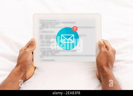 Afrikanischer Mann Liest E-Mail-Nachrichten Auf Tablet Liegend Im Schlafzimmer Stockfoto