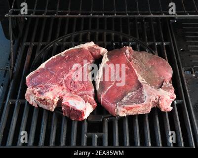Zwei rohe Porterhouse T-Bone Steaks auf einem Grill von einem Gasgrill Stockfoto