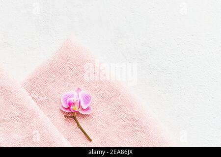 Rolled rosa Handtuch und Orchidee Blume auf weißem Beton Hintergrund. Minimalistischer skandinavischer Stil. SPA, Hygiene, Wellness-Wohlbefinden, Körperpflege-Konzept. Stockfoto